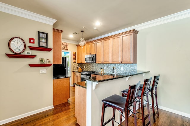 kitchen with a breakfast bar area, a peninsula, appliances with stainless steel finishes, tasteful backsplash, and pendant lighting