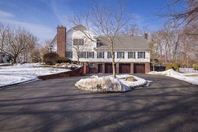 view of front of house with brick siding, driveway, a chimney, and an attached garage