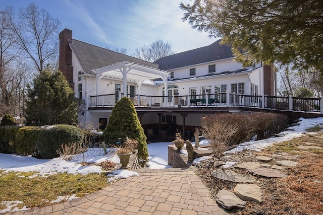 snow covered rear of property featuring a patio, a chimney, a wooden deck, and a pergola