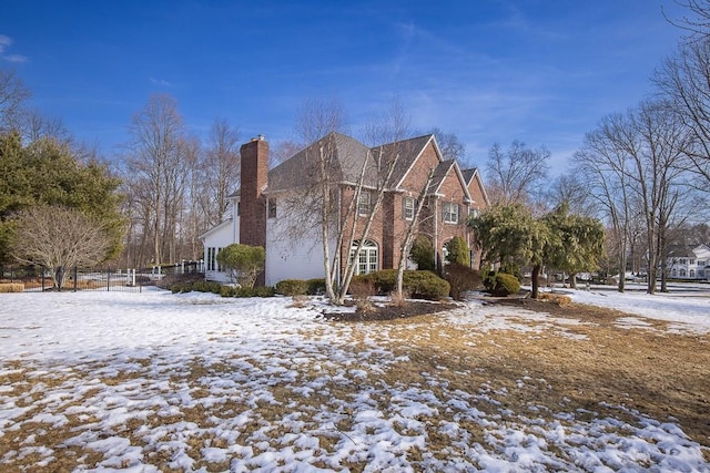 view of snowy exterior with brick siding and a chimney