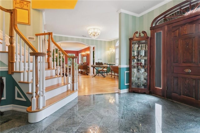 entryway featuring arched walkways, stairway, ornamental molding, ornate columns, and wallpapered walls