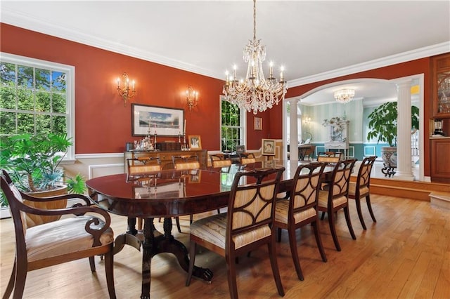 dining space with decorative columns, arched walkways, a chandelier, and wood finished floors