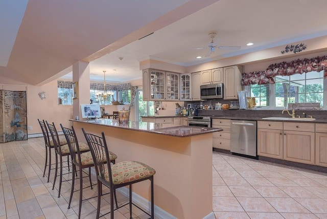 kitchen with appliances with stainless steel finishes, a breakfast bar area, a sink, and glass insert cabinets