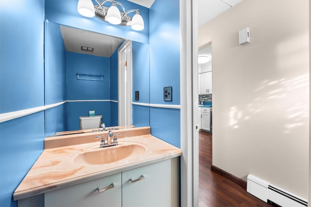 half bathroom featuring a baseboard radiator, toilet, wood finished floors, and vanity