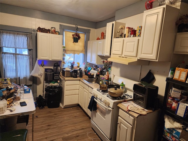 kitchen with white range with gas stovetop, white cabinetry, light countertops, and a sink