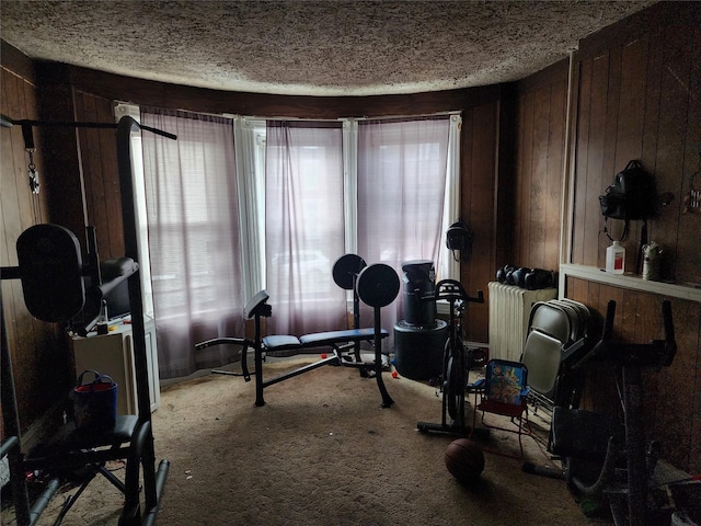 workout area with a textured ceiling, wood walls, and carpet flooring