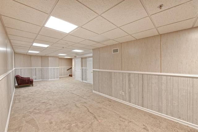 finished basement with carpet floors, wooden walls, visible vents, and a paneled ceiling