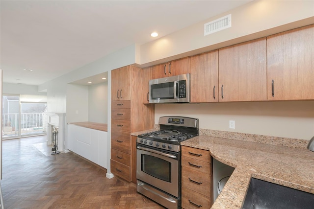 kitchen featuring stainless steel appliances, a fireplace, a sink, visible vents, and light stone countertops