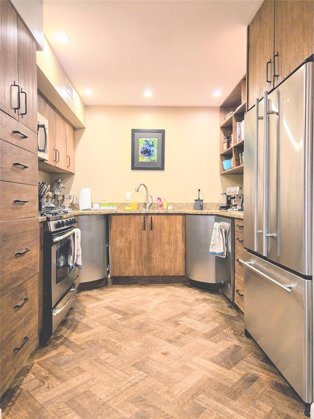 kitchen with light stone counters, brown cabinets, stainless steel appliances, open shelves, and a sink