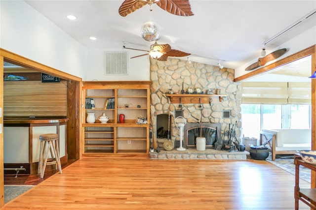 living area featuring visible vents, lofted ceiling, ceiling fan, wood finished floors, and a fireplace