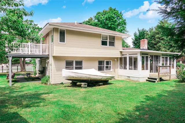 back of property featuring a sunroom, a chimney, a lawn, and a wooden deck