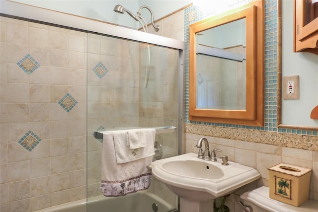 bathroom with toilet, tile walls, combined bath / shower with glass door, and a sink