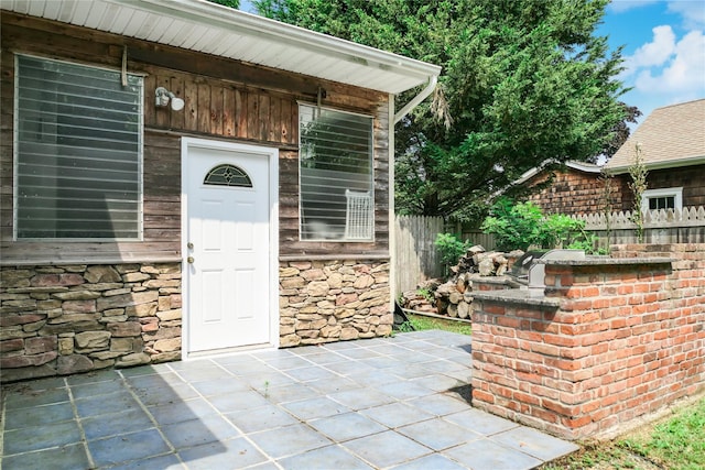 property entrance with a patio, stone siding, and fence