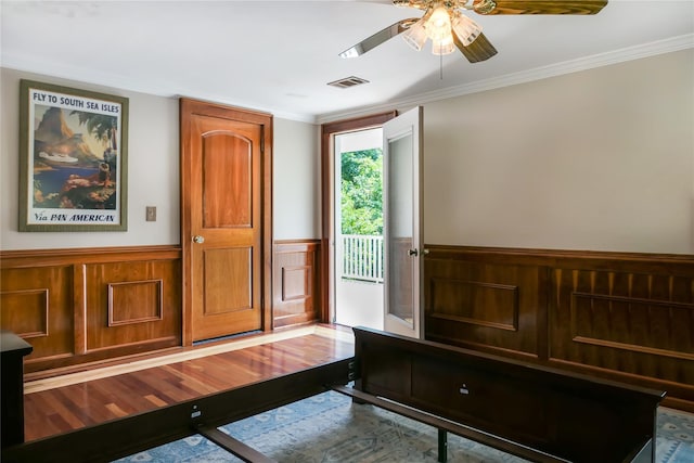 entryway featuring ceiling fan, wood finished floors, visible vents, wainscoting, and crown molding