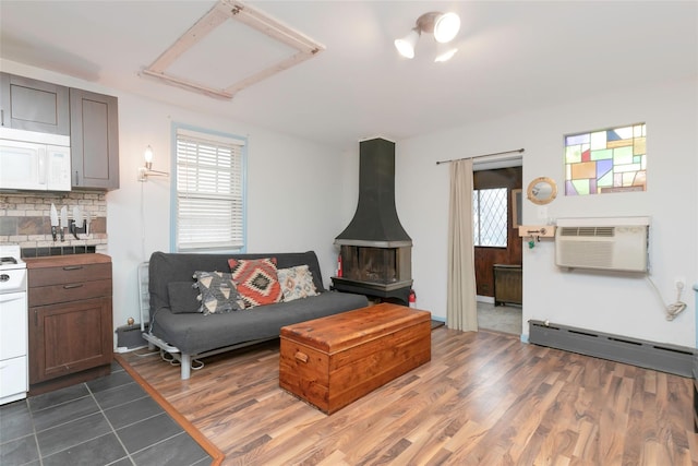 living room with dark wood finished floors, a wood stove, a wall mounted air conditioner, and baseboard heating