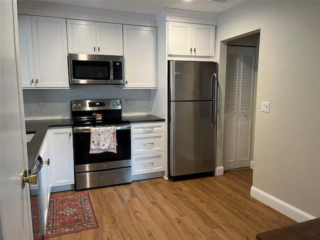 kitchen with light wood finished floors, tasteful backsplash, dark countertops, appliances with stainless steel finishes, and white cabinetry