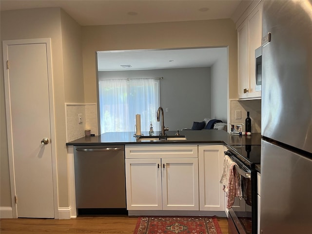 kitchen featuring stainless steel appliances, dark countertops, light wood-style floors, white cabinets, and a sink