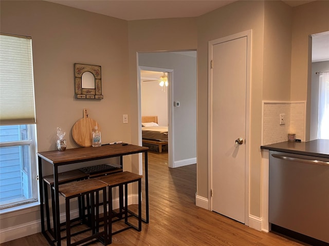 kitchen featuring dark countertops, decorative backsplash, stainless steel dishwasher, wood finished floors, and baseboards