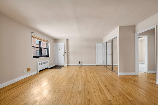 unfurnished living room with baseboards, radiator heating unit, and light wood-style floors