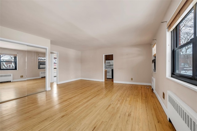 unfurnished living room featuring baseboards, light wood finished floors, and radiator