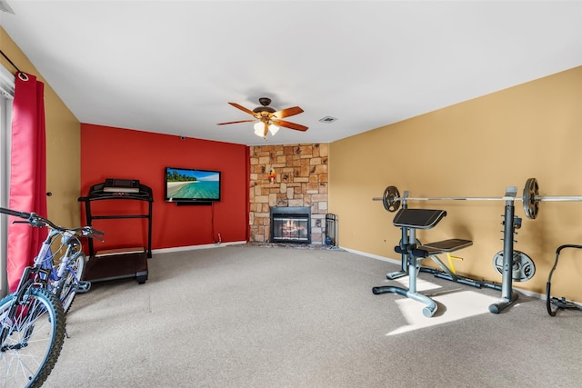 workout area featuring baseboards, visible vents, a ceiling fan, carpet flooring, and a stone fireplace