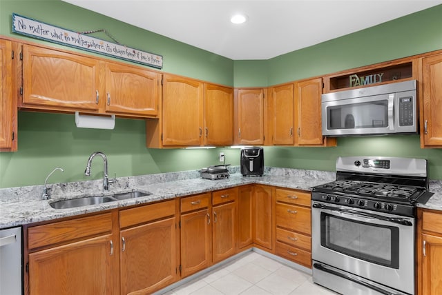 kitchen with brown cabinets, appliances with stainless steel finishes, light stone counters, and a sink