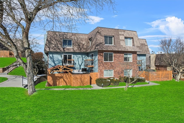 exterior space with brick siding, a yard, fence, and mansard roof