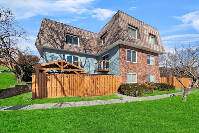 view of front of property with brick siding, mansard roof, fence, a gazebo, and a front yard