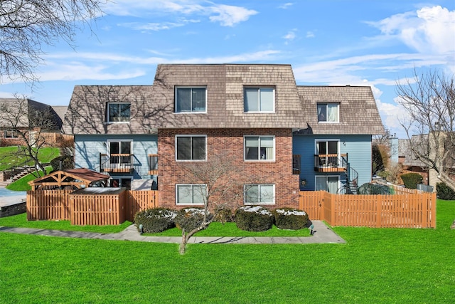 view of front of home featuring a balcony, a front yard, mansard roof, and brick siding