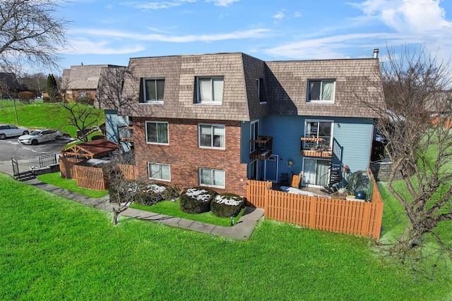 back of house featuring a yard, brick siding, fence, and mansard roof