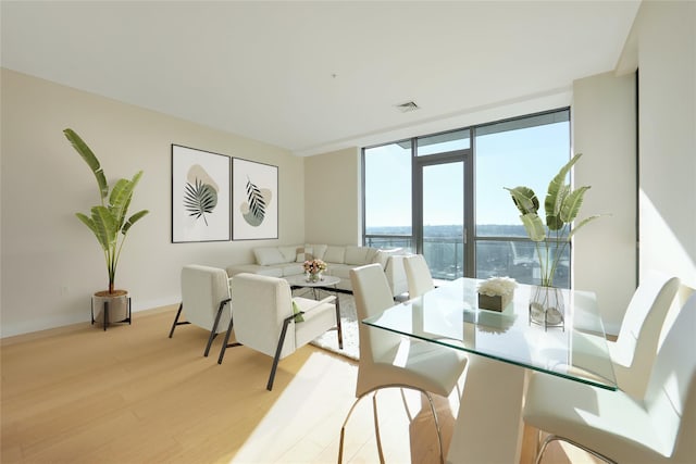 dining area featuring light wood-style floors, floor to ceiling windows, visible vents, and a water view