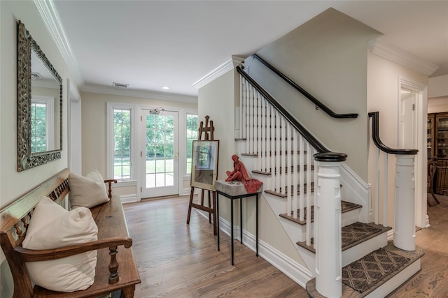 staircase with ornamental molding, visible vents, baseboards, and wood finished floors