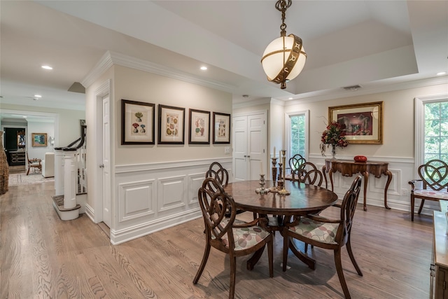 dining space featuring light wood-style flooring, recessed lighting, a wainscoted wall, a decorative wall, and ornamental molding