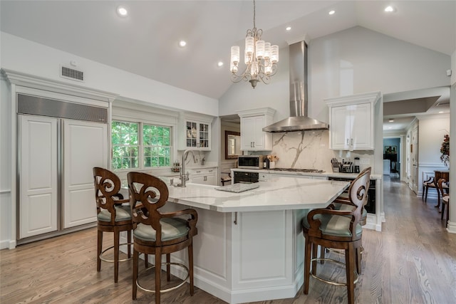 kitchen featuring a spacious island, white cabinets, wall chimney exhaust hood, glass insert cabinets, and pendant lighting