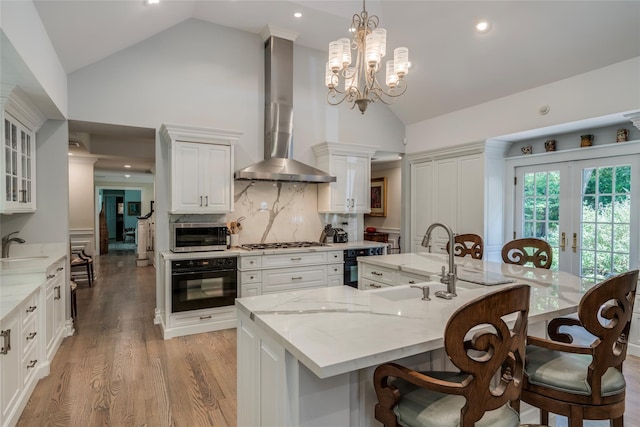 kitchen with appliances with stainless steel finishes, a large island with sink, wall chimney range hood, and glass insert cabinets