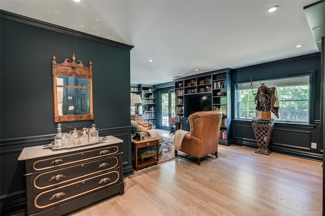 sitting room with ornamental molding, light wood-type flooring, wainscoting, and a decorative wall