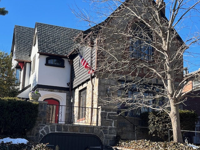 view of side of home featuring a shingled roof, stone siding, and stucco siding