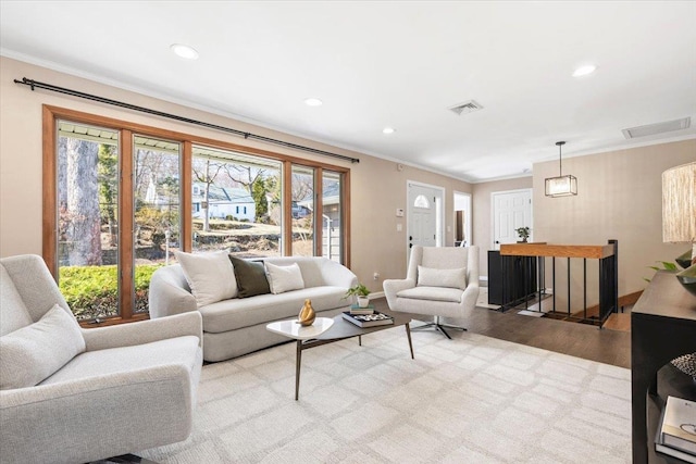 living room with visible vents, plenty of natural light, crown molding, and wood finished floors