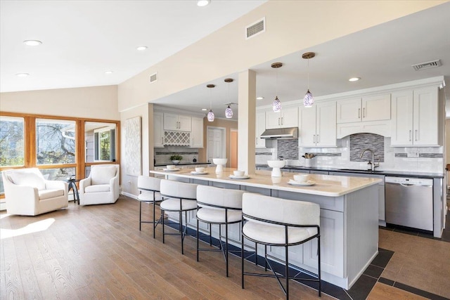 kitchen featuring visible vents, a sink, vaulted ceiling, under cabinet range hood, and stainless steel dishwasher