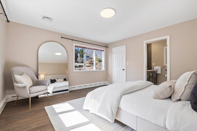 bedroom with wood finished floors, visible vents, baseboards, ensuite bathroom, and a baseboard heating unit