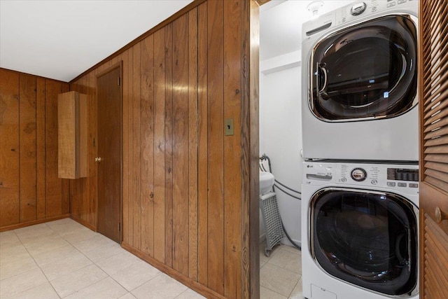 clothes washing area with light tile patterned floors, wooden walls, laundry area, and stacked washing maching and dryer