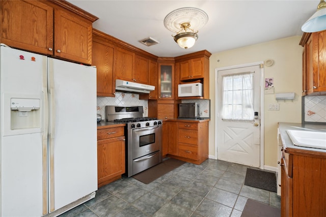 kitchen featuring visible vents, glass insert cabinets, brown cabinetry, white appliances, and under cabinet range hood