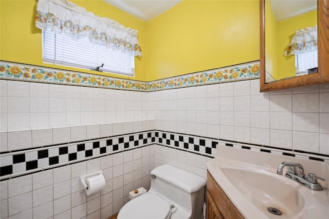 bathroom featuring toilet, a wainscoted wall, tile walls, and vanity