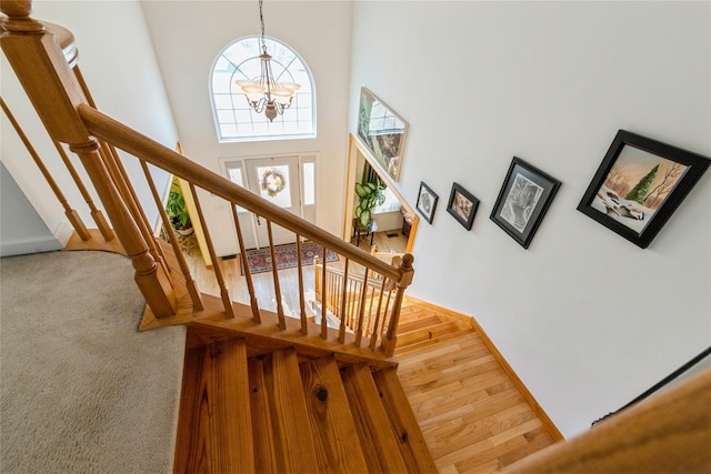 staircase with baseboards, a high ceiling, wood finished floors, and an inviting chandelier