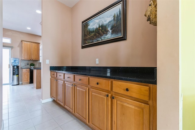 kitchen with light tile patterned floors, recessed lighting, backsplash, brown cabinetry, and dark stone countertops