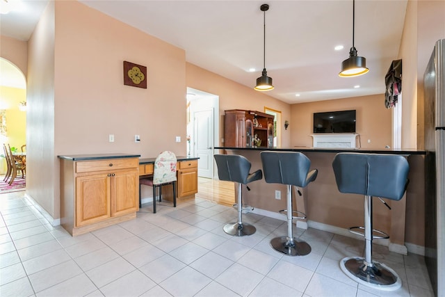 kitchen with light tile patterned floors, arched walkways, dark countertops, a kitchen breakfast bar, and hanging light fixtures