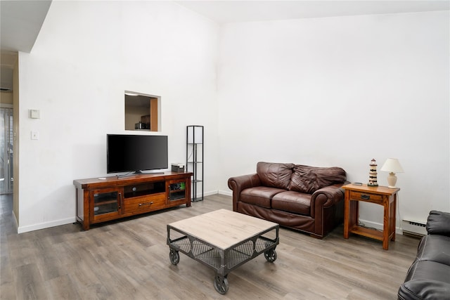 living area with a baseboard heating unit, baseboards, and wood finished floors