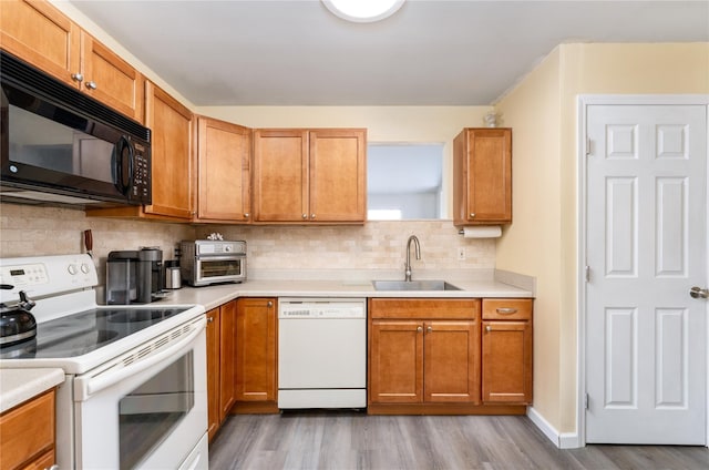 kitchen featuring white appliances, a sink, light countertops, light wood-type flooring, and backsplash