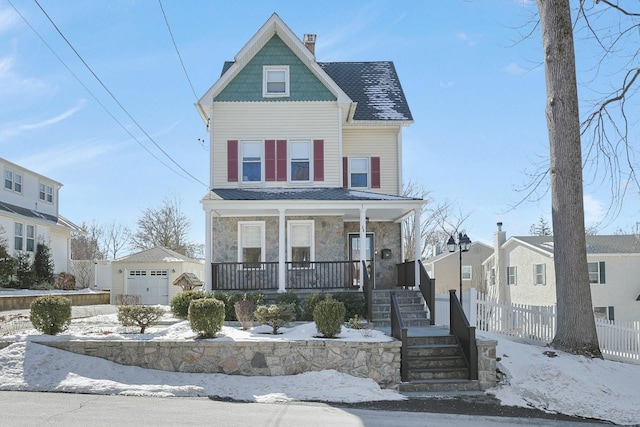 victorian house featuring a porch, a garage, an outdoor structure, stone siding, and a chimney