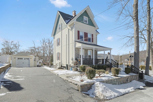 view of front of house featuring a porch, aphalt driveway, a garage, an outdoor structure, and a chimney